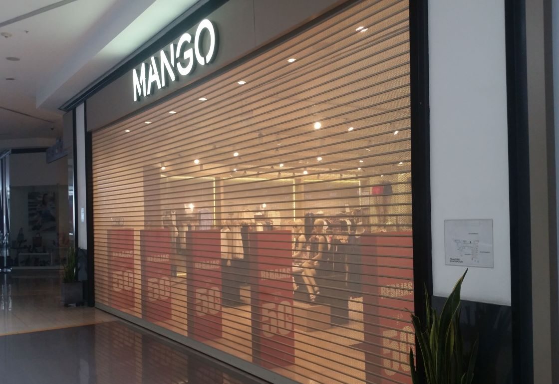 Puerta enrollable metálica Full Vision instalada en tienda Mango dentro de centro comercial, con microperforado que permite visibilidad y seguridad.