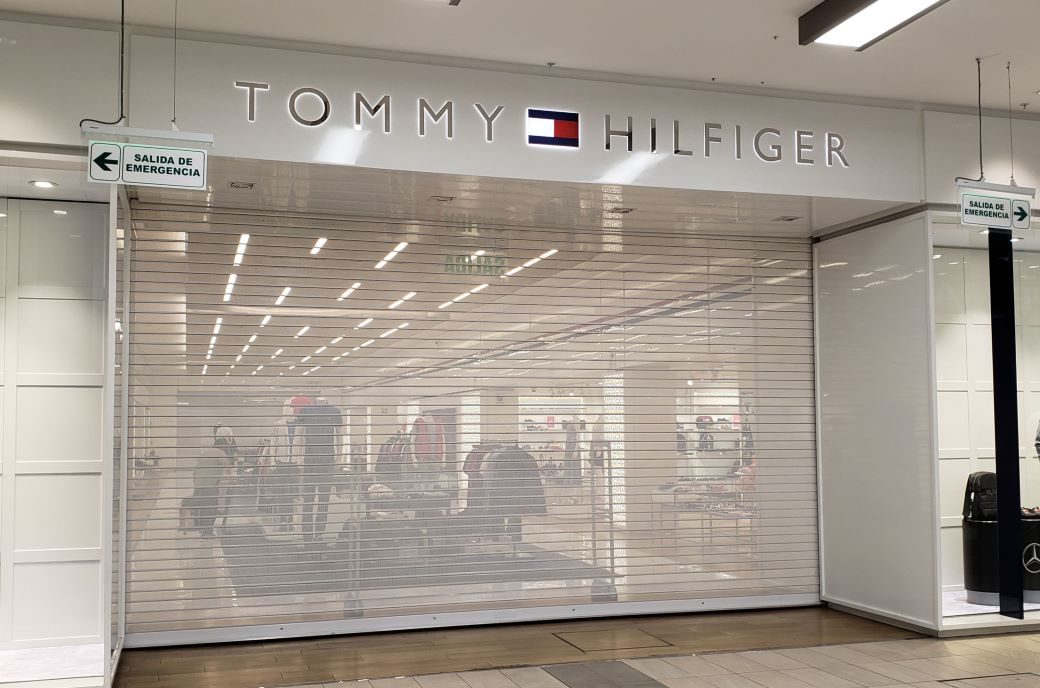 Puerta enrollable metálica Full Vision instalada en tienda Tommy Hilfiger dentro de centro comercial, con microperforado que permite visibilidad continua y protección del local.