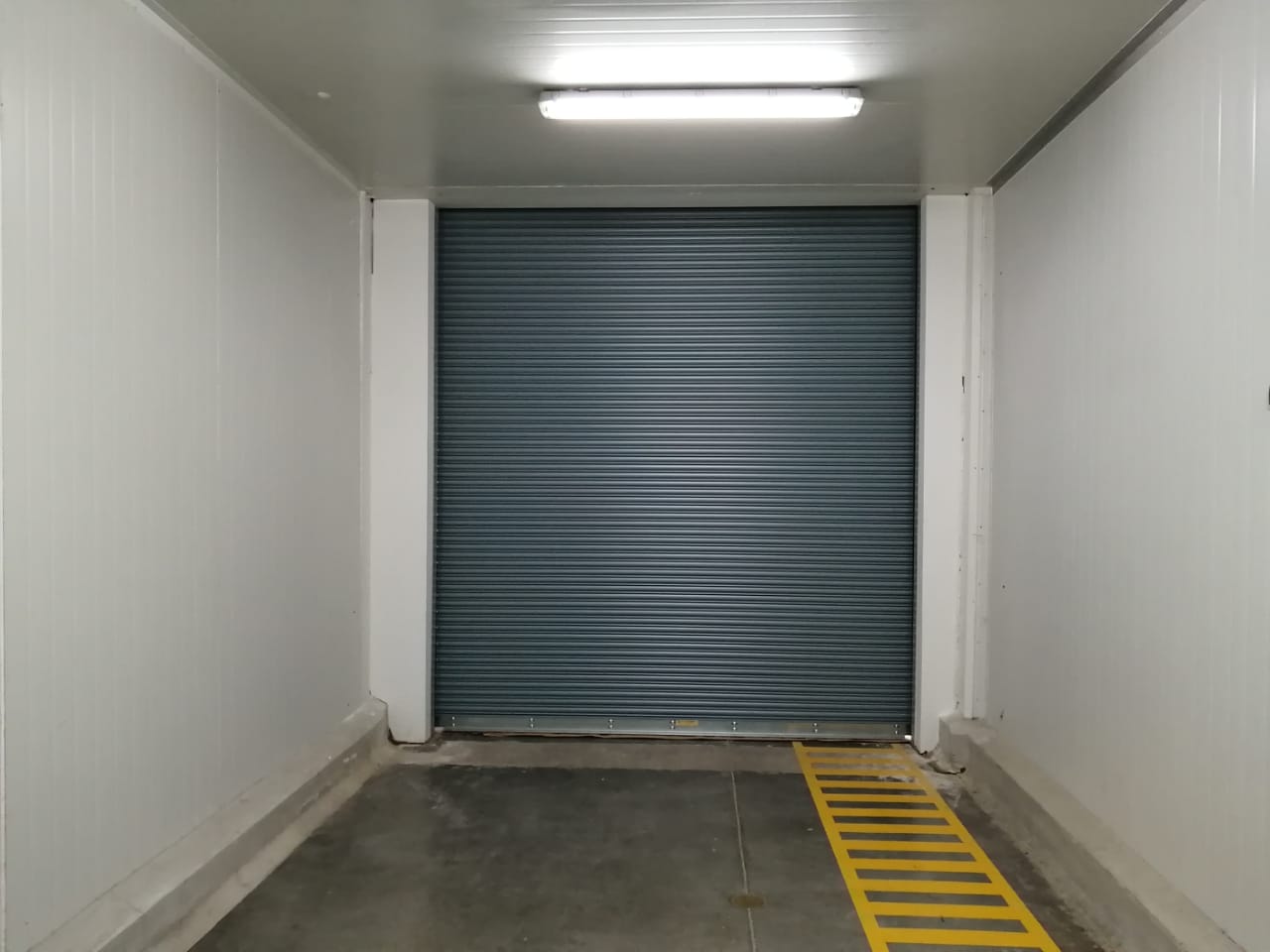 Puerta enrollable cortafuego en color gris instalada en acceso de almacén logístico, diseñada para activarse automáticamente ante emergencias, creando una barrera que sectoriza el incendio y reduce la propagación del fuego.