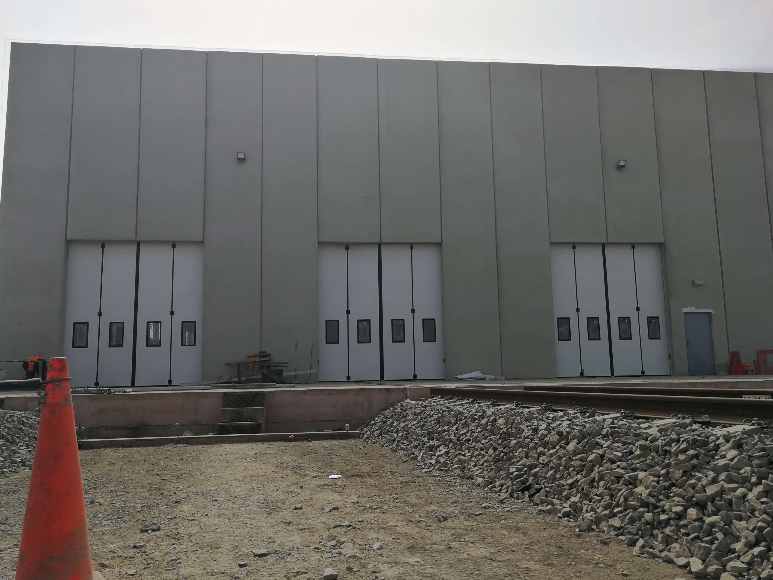 Puertas abatibles industriales instaladas en entorno exterior con materiales industriales, con apertura lateral y paneles insulados articulados que aportan resistencia, estabilidad y facilidad de uso.