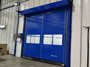 Puerta rápida de PVC FastZipp autoreparable en color azul, instalada en área logística, con sistema que restablece el paño tras colisiones y favorece la continuidad del flujo operativo.