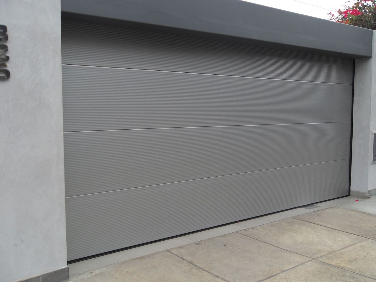 Puerta seccional de garaje en color gris instalada en edificio residencial, con apertura vertical que optimiza el espacio y diseño que cumple normativas municipales sin invadir la vereda durante su operación.