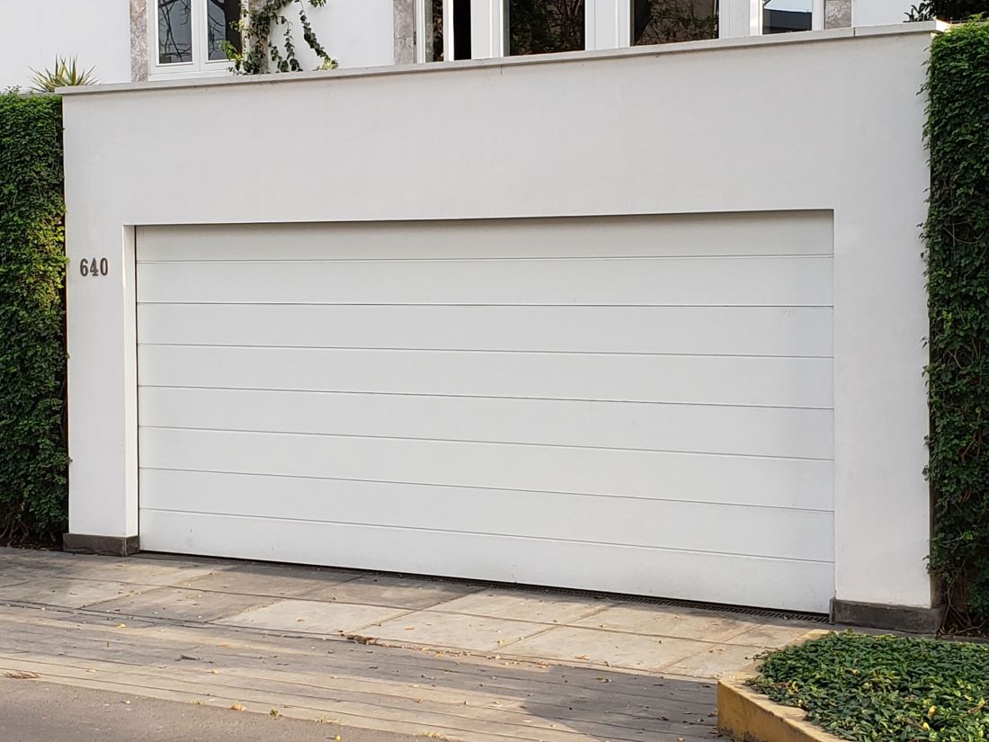 Puerta seccional de garaje en color blanco instalada en vivienda, con apertura vertical que optimiza el espacio, acabado de calidad y diseño que se integra a la estética del hogar.