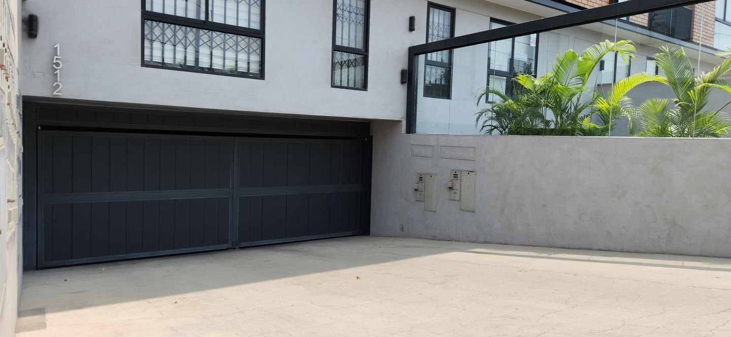 Puerta batiente de garaje en color negro instalada en edificio residencial, construida con acero galvanizado que ofrece resistencia, seguridad y un desempeño confiable en el ingreso vehicular.