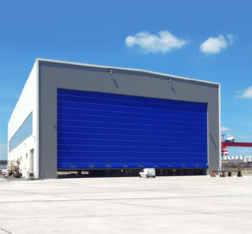 Puerta plegable de PVC para hangar aeronáutico de gran dimensión, con bastidores transversales de aluminio que aseguran estabilidad estructural frente al viento, evitando deformaciones y garantizando operación segur