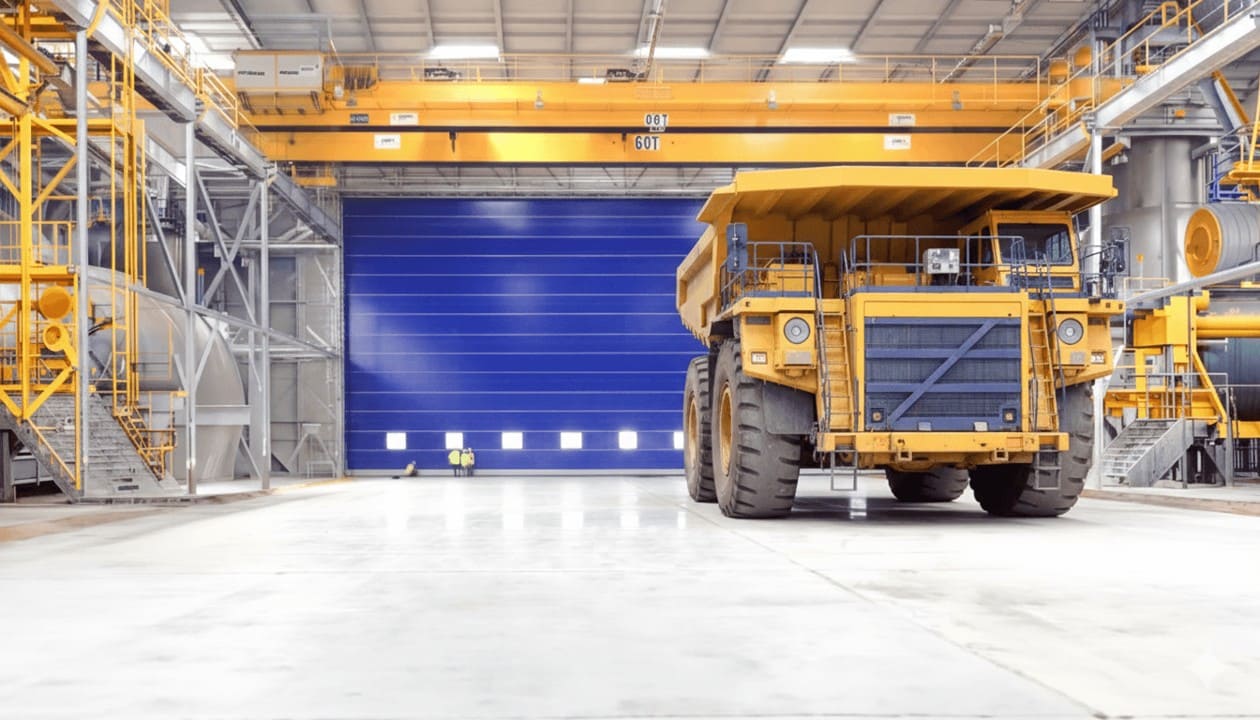Puerta plegable de PVC para hangares instalada en almacén industrial de gran dimensión, con apertura libre total para maquinaria pesada, alta resistencia al viento y operación confiable en entornos exigentes.
