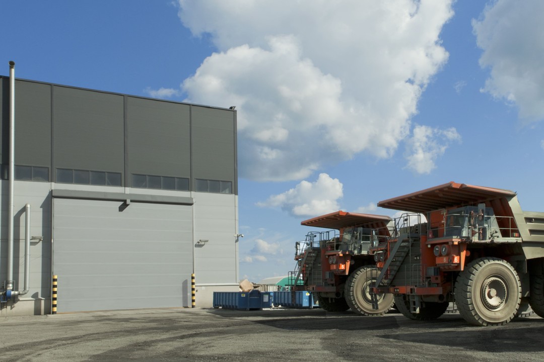 Puerta plegable de PVC para hangar minero con maquinaria pesada de gran escala, sin límite práctico de tamaño y alta resistencia al viento, fabricada con doble lona técnica de PVC resistente al rasgado para entornos exigentes.