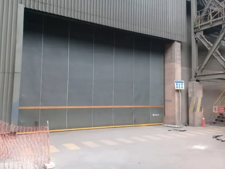 Puerta enrollable de caucho instalada en almacén minero con alta polución, destacando su resistencia a condiciones corrosivas y su desempeño en entornos industriales exigentes.