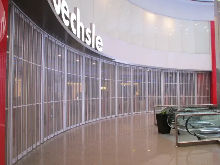 Puerta plegable Cassafold instalada en tienda Oechsle dentro de centro comercial, con sistema modular que optimiza el espacio y permite apertura lateral eficiente.