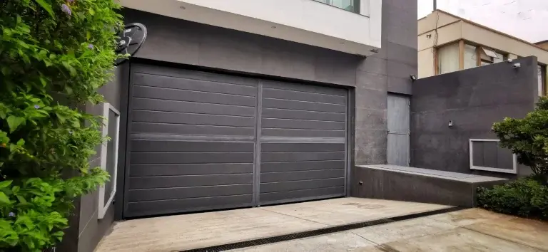 Puerta batiente de garaje en color negro instalada en vivienda, fabricada con estructura de acero galvanizado que brinda durabilidad, seguridad y funcionamiento confiable para ingreso vehicular.