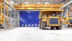 Puerta plegable de PVC para hangares instalada en almacén industrial de gran dimensión, con apertura libre total para maquinaria pesada, alta resistencia al viento y operación confiable en entornos exigentes.