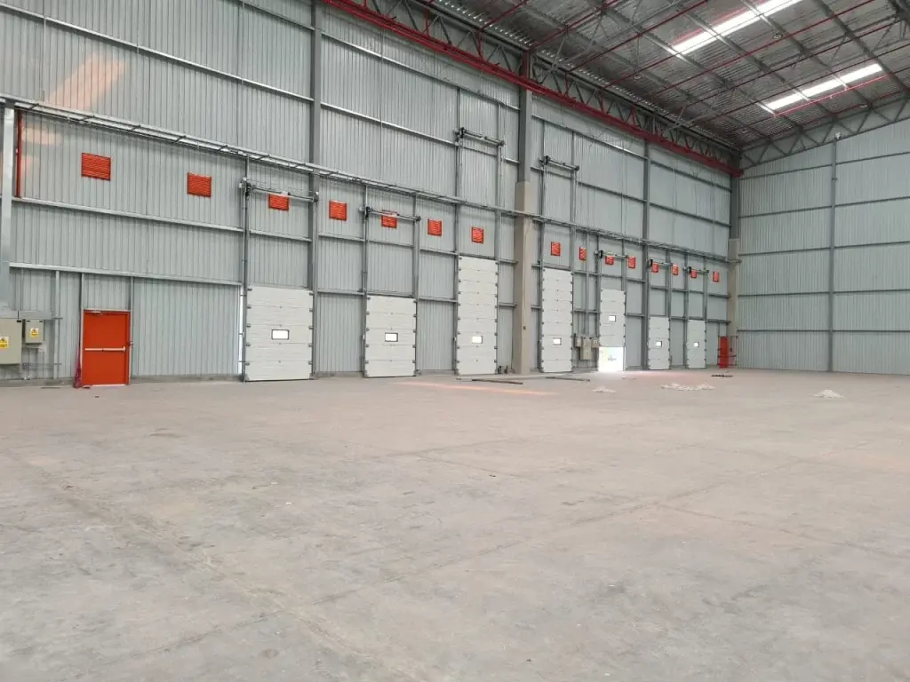 Puertas seccionales industriales en color blanco de distintos tamaños instaladas en almacén, con paneles tipo sándwich de 40 mm con núcleo de poliuretano que aportan aislamiento térmico y acústico.