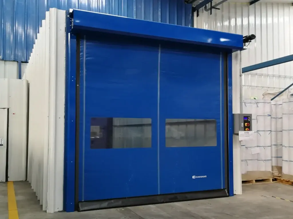 Puerta rápida de PVC FastZipp autoreparable en color azul, instalada en entorno logístico, con sistema que recupera el paño tras impactos y mantiene la continuidad operativa.