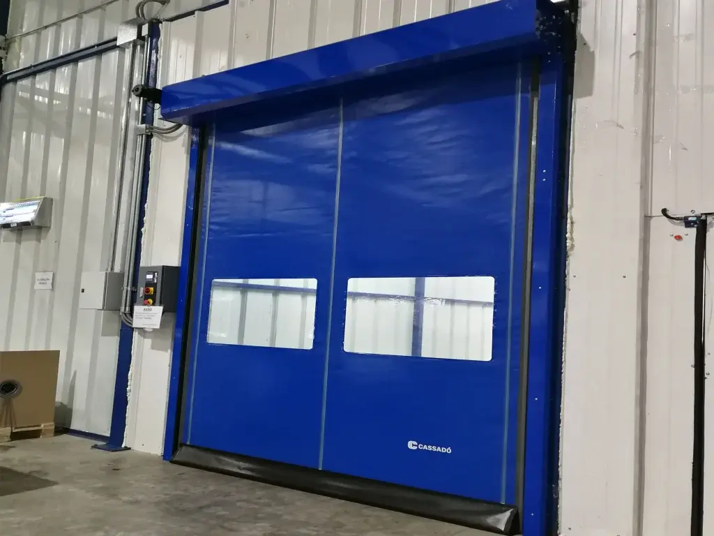 Puerta rápida de PVC FastZipp autoreparable en color azul, instalada en área logística, con sistema que restablece el paño tras colisiones y favorece la continuidad del flujo operativo.