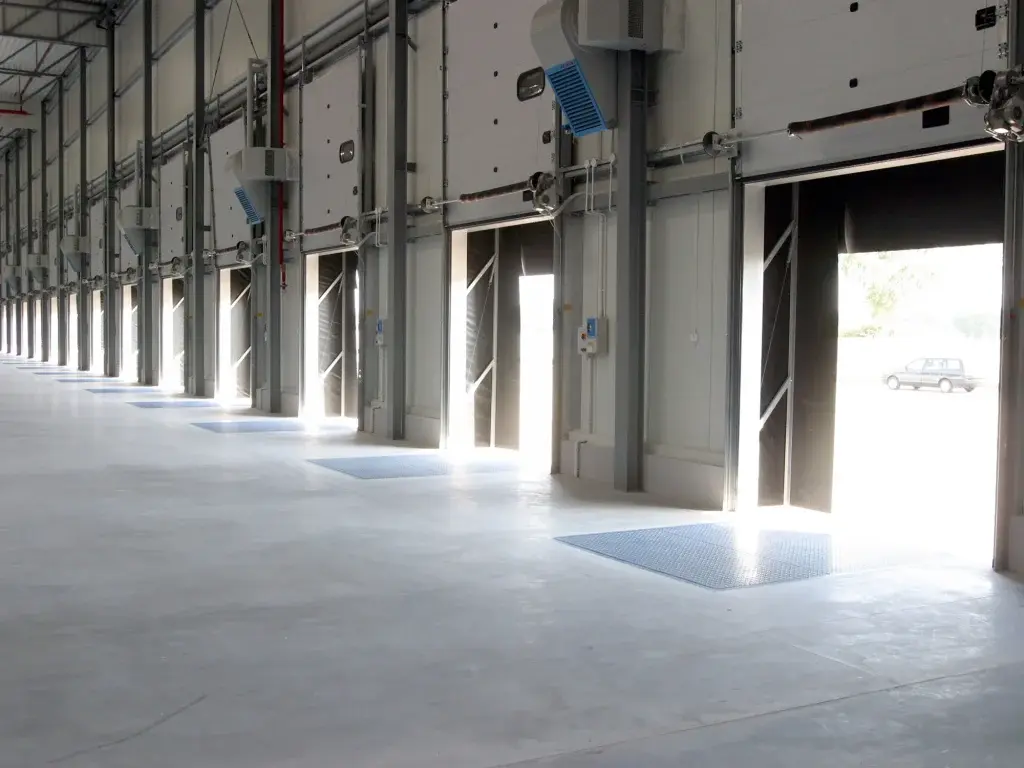 Puertas seccionales industriales en color blanco abiertas en entorno logístico, facilitando el flujo de carga y descarga, con sistema confiable para operaciones en centros de distribución.